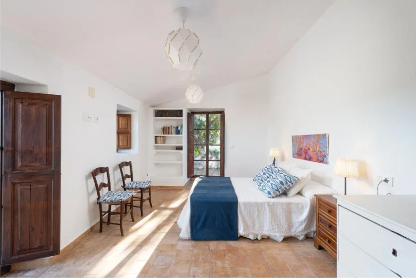 Un dormitorio luminoso con una cama, dos sillas y una puerta acristalada.