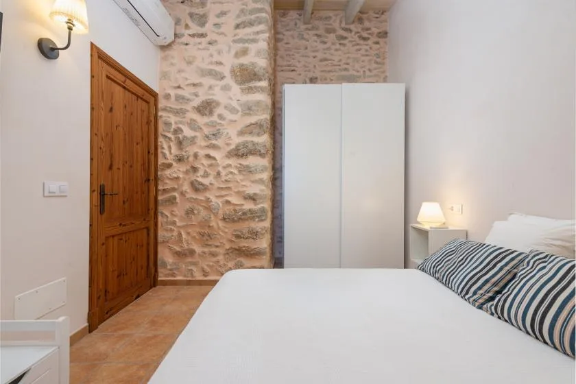 Un dormitorio con una cama, un armario y paredes de piedra vista.