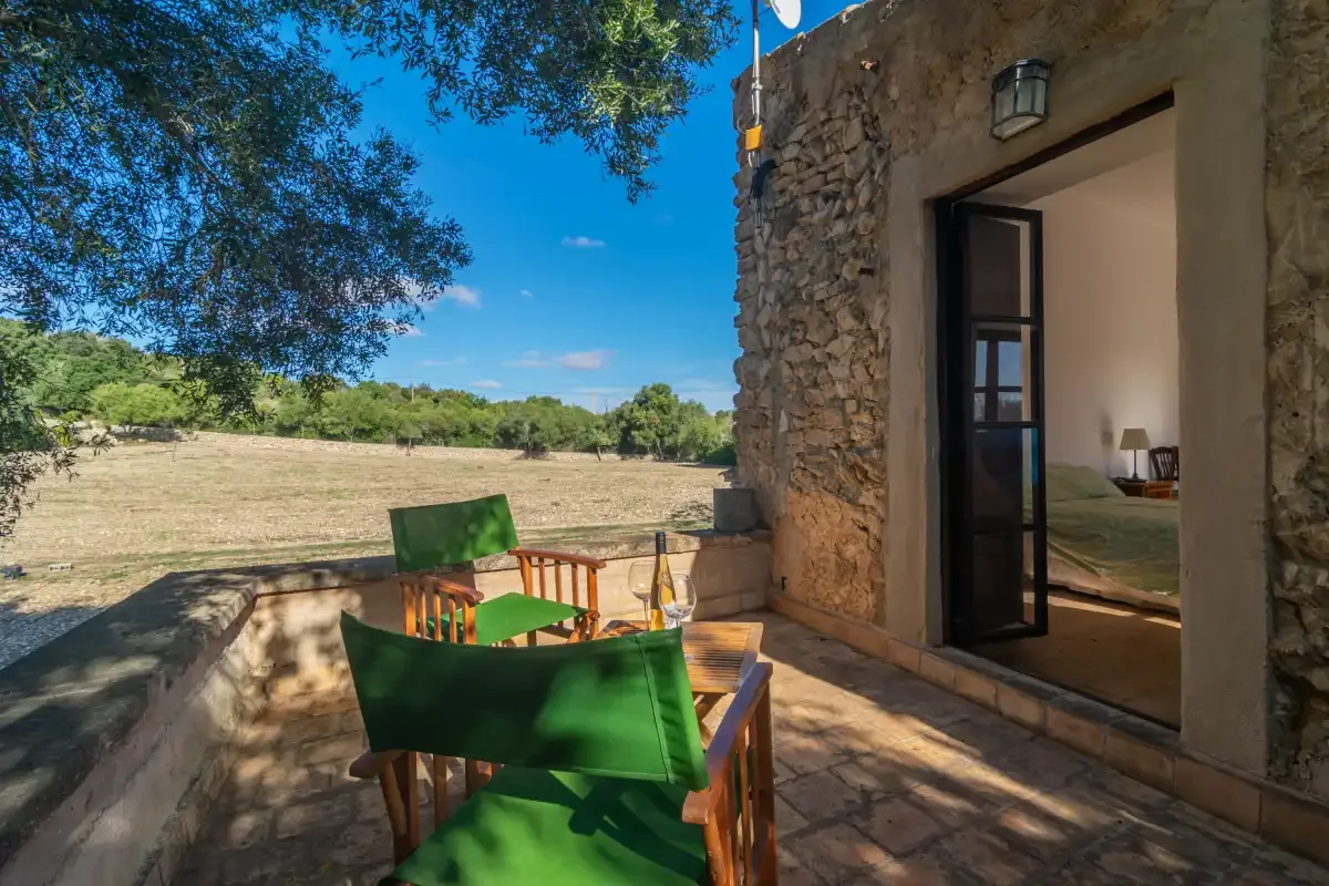 Una terraza de piedra con asientos verdes da a un campo abierto.