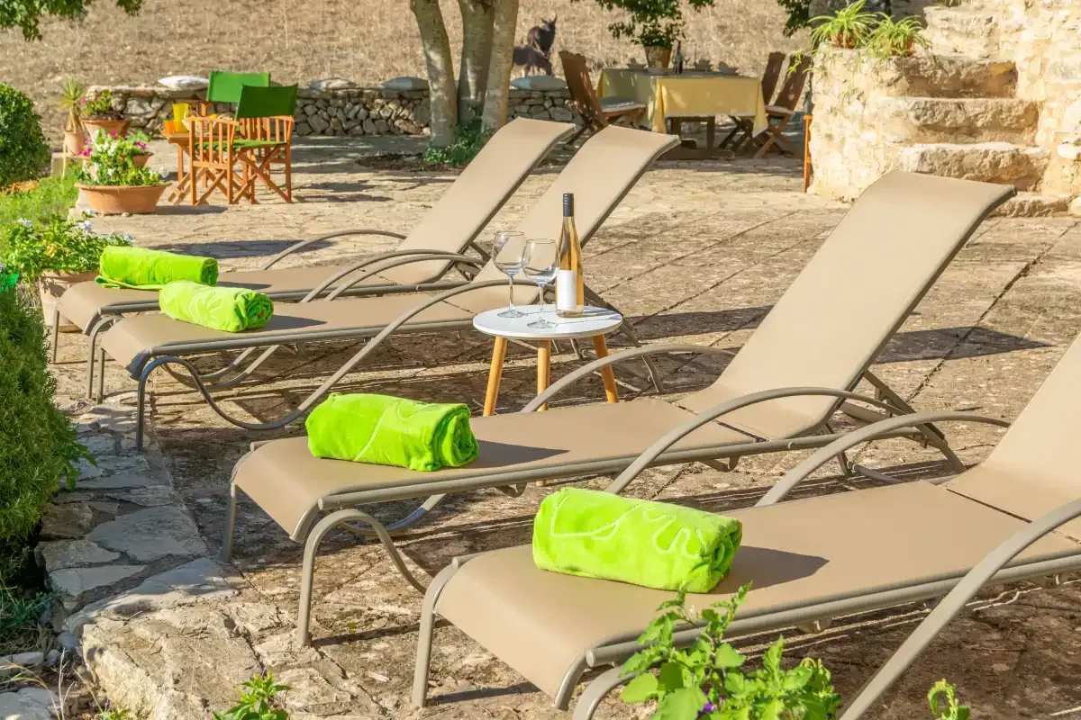 Una terraza de piedra soleada con asientos reclinables y toallas verdes.