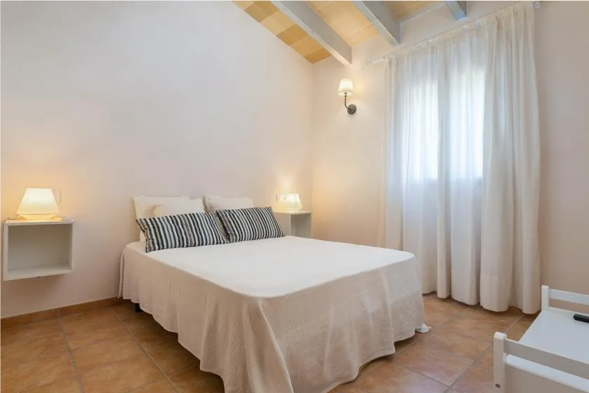 Un dormitorio con una cama bien tendida junto a una ventana con cortinas.