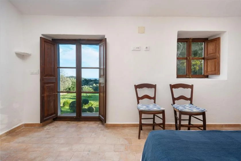 Una habitación sencilla con dos sillas de madera, ventanas abiertas y vistas a zonas verdes.