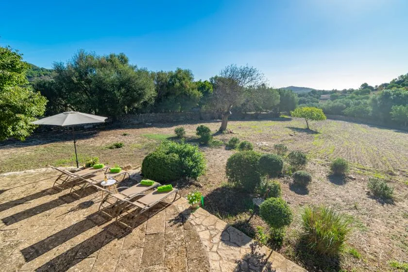 An outdoor patio with lounge seating overlooks a landscaped garden and wooded hills.