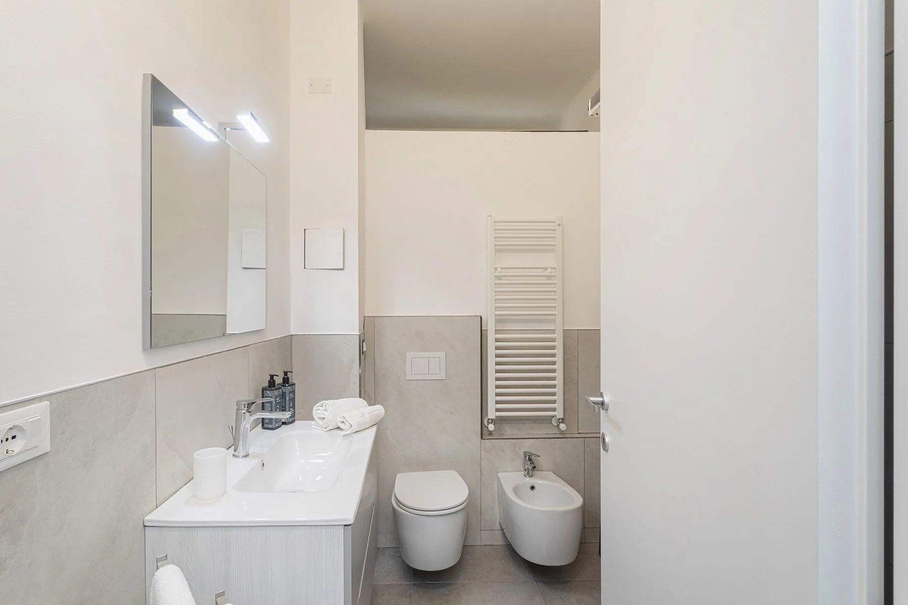 A bright bathroom with a sink, mirror, toilet, and bidet.