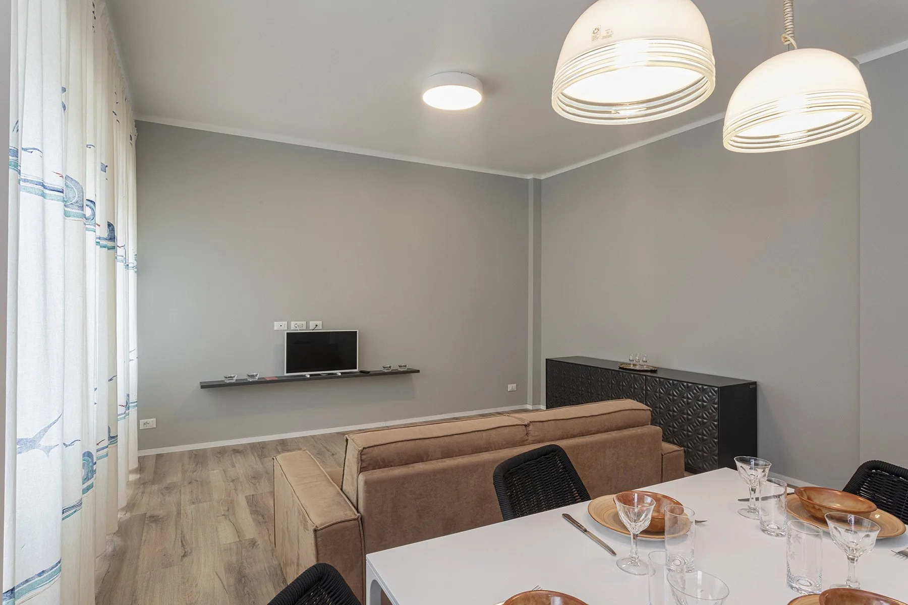 A living and dining area with a sofa, dining table, and wall-mounted television.