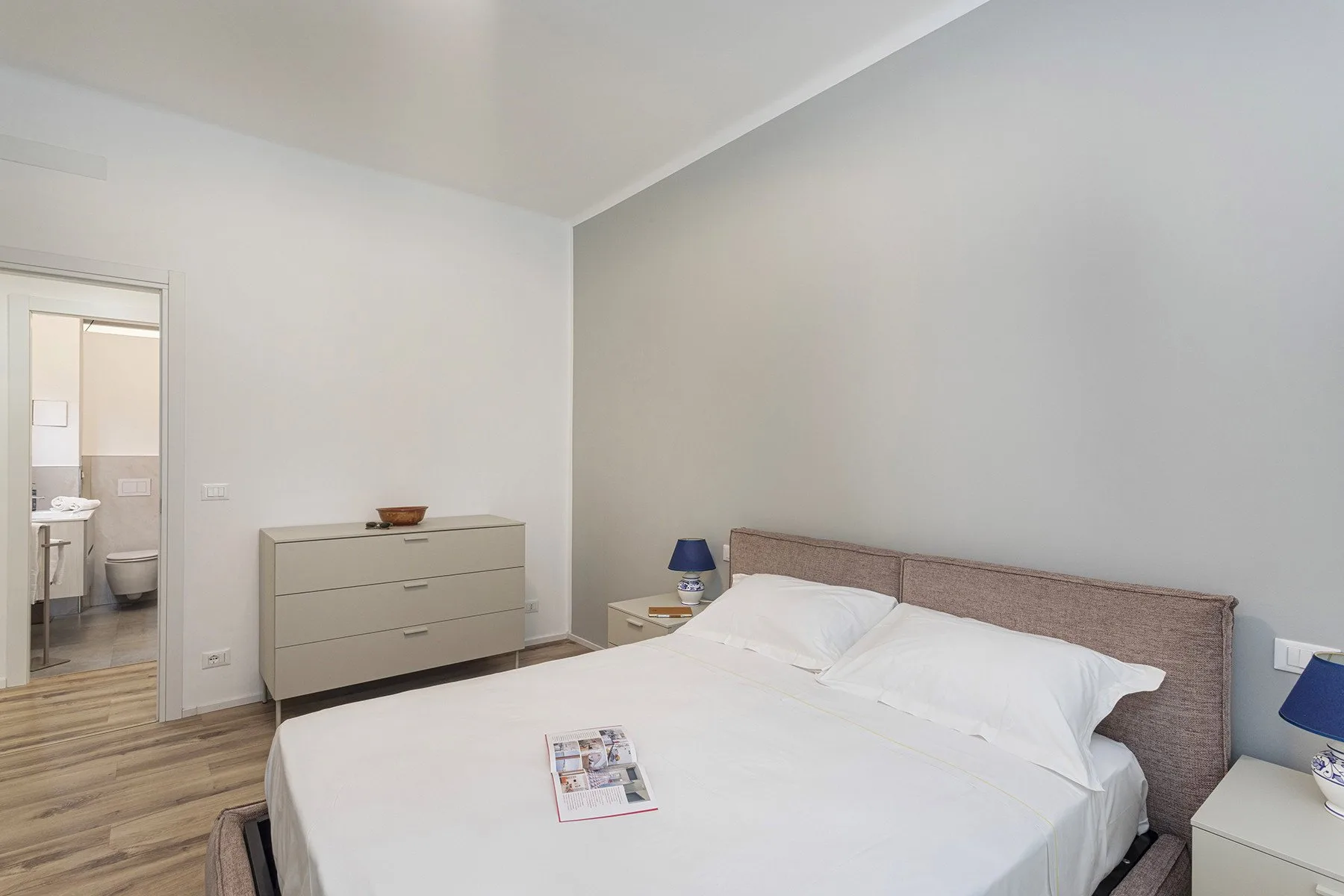 A bright bedroom with a neatly made bed and a dresser.