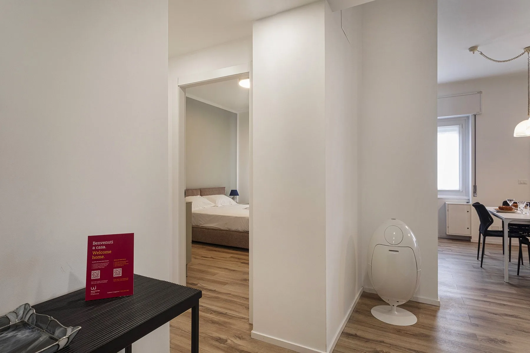 A bright apartment interior with a toilet, a bedroom doorway, and dining seating.