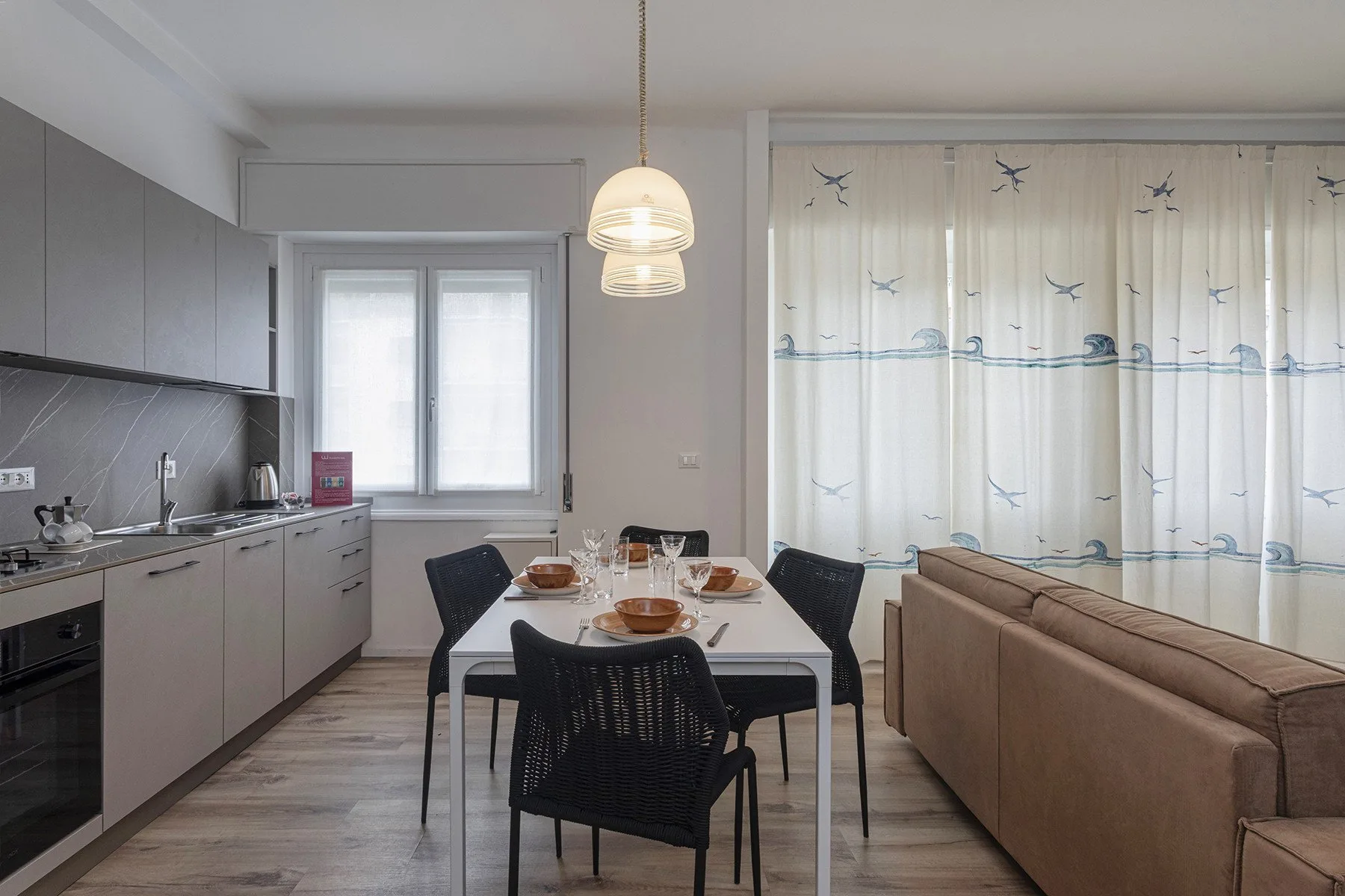 A dining table sits between the kitchen and living area, beside a curtained window.