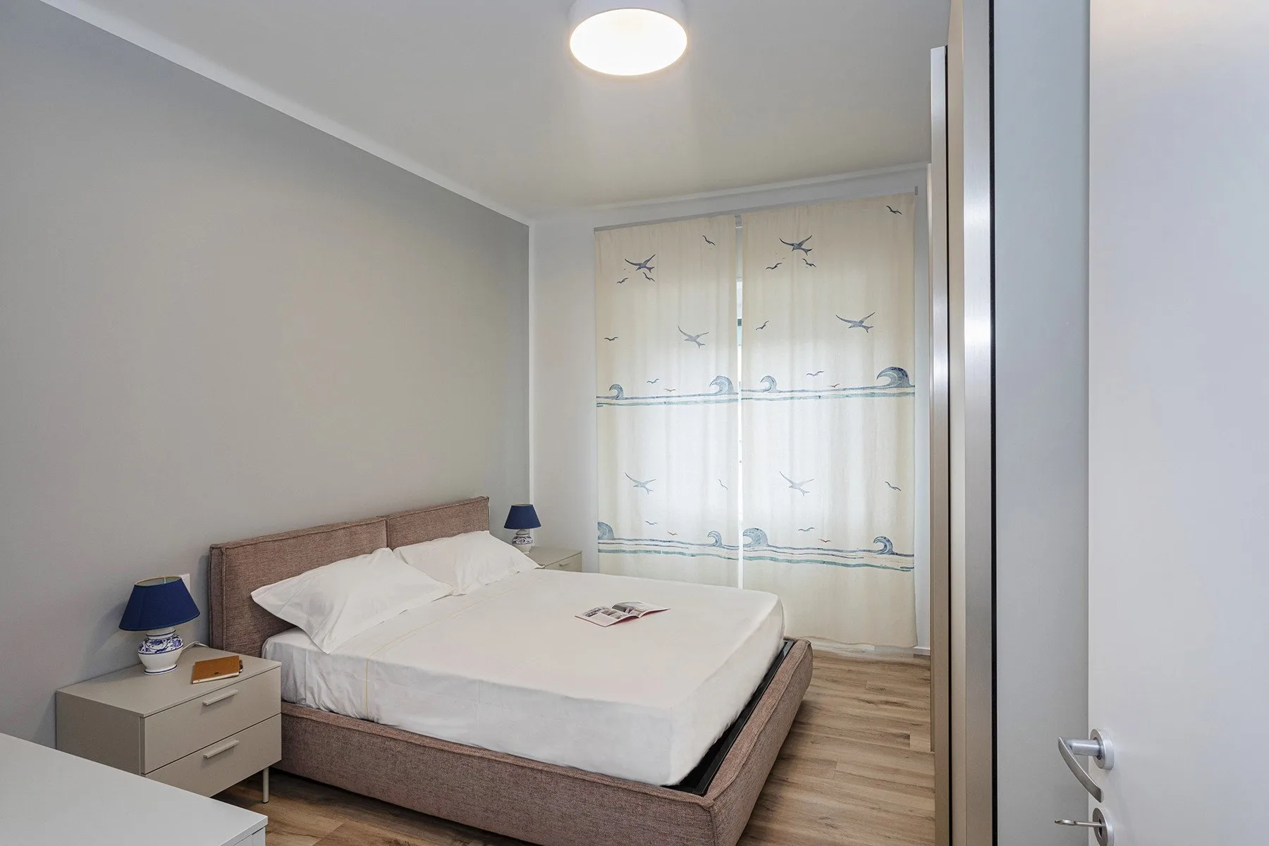 A bedroom with a double bed, bedside table, and patterned curtains.