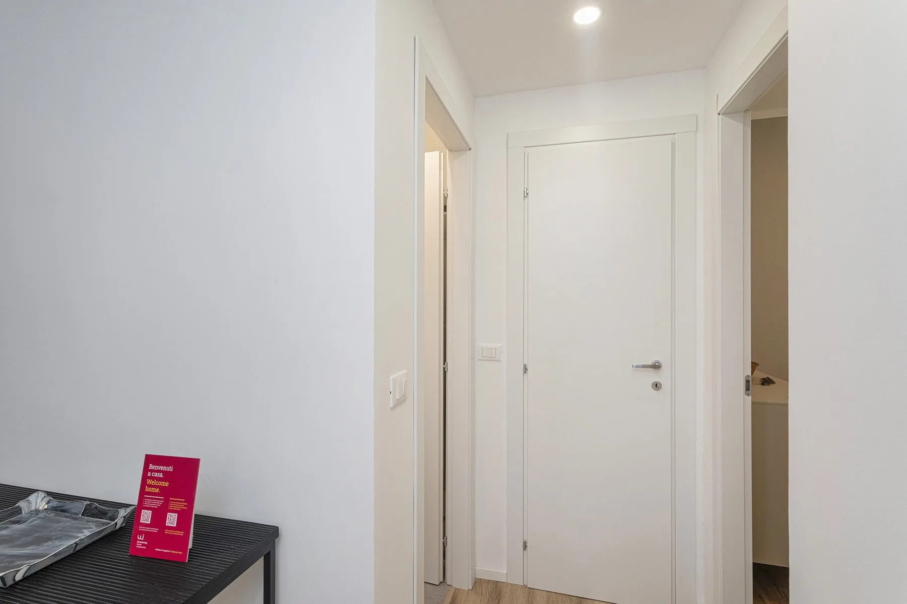 A white hallway with a closed door and openings to adjoining rooms.