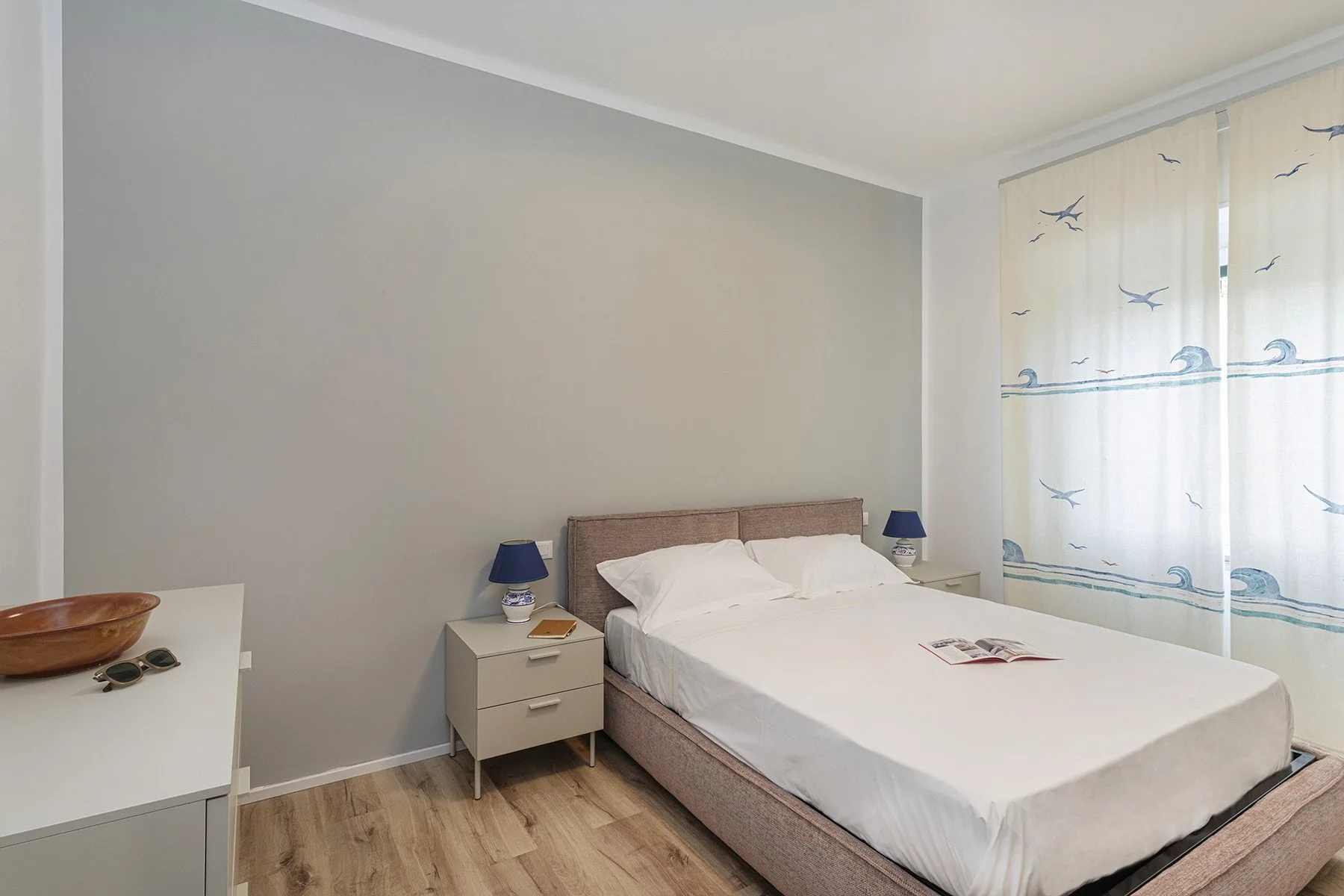 A bedroom with a double bed, bedside tables, and patterned curtains.