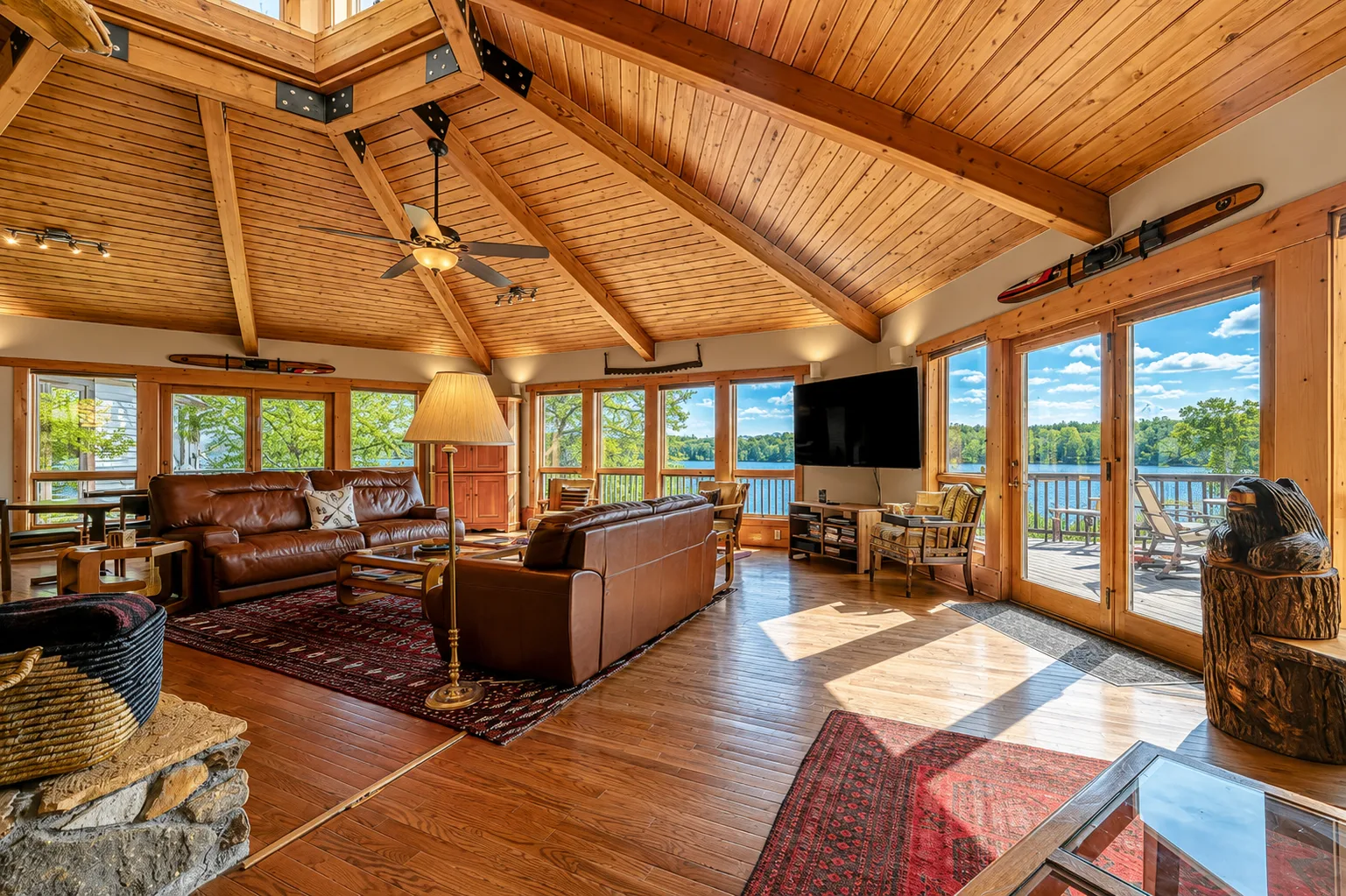 Una amplia sala de estar con techo de vigas de madera y grandes ventanas con vista al lago.