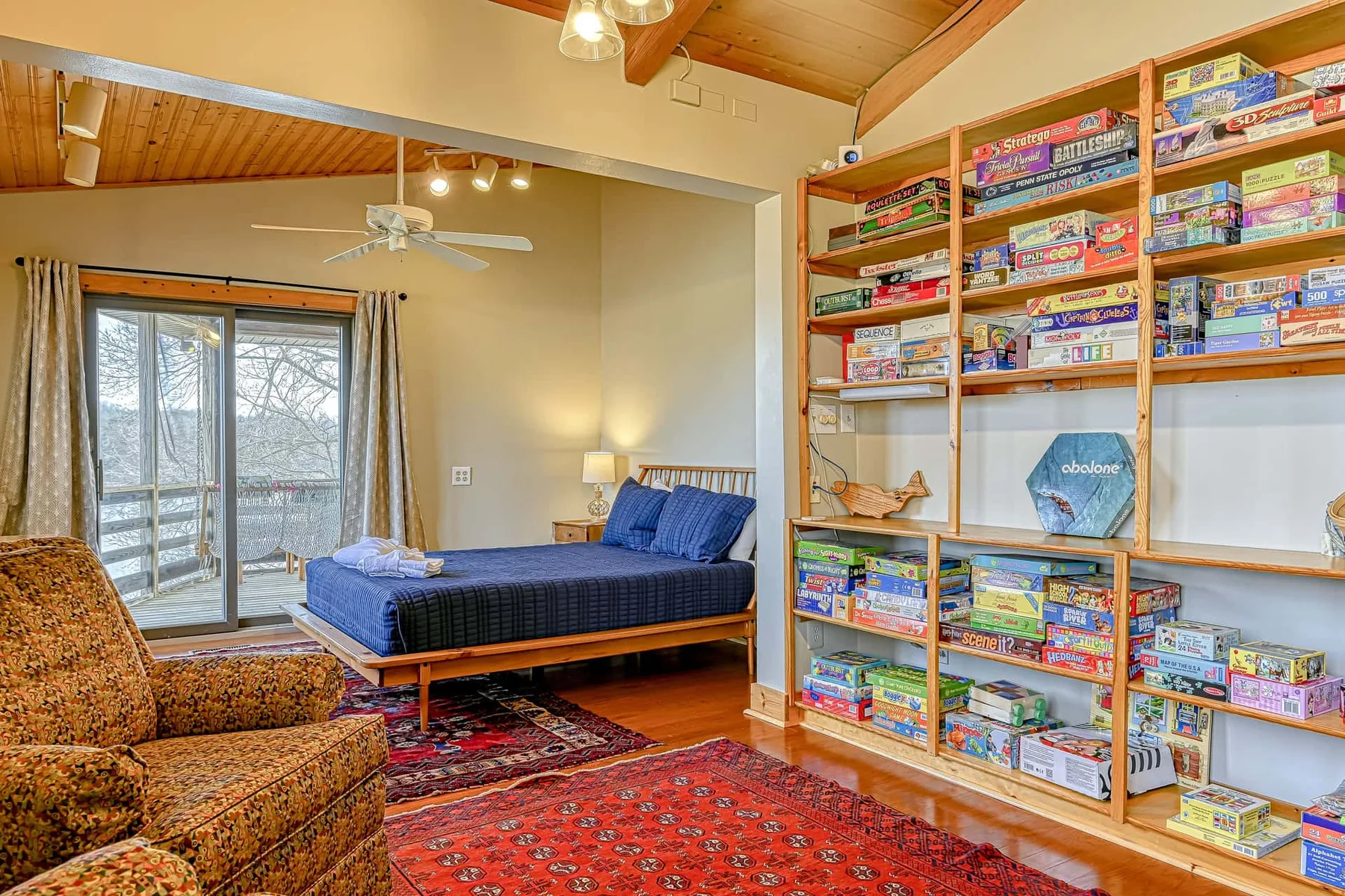 Un dormitorio con una cama azul, alfombras estampadas y estantes con juegos de mesa.