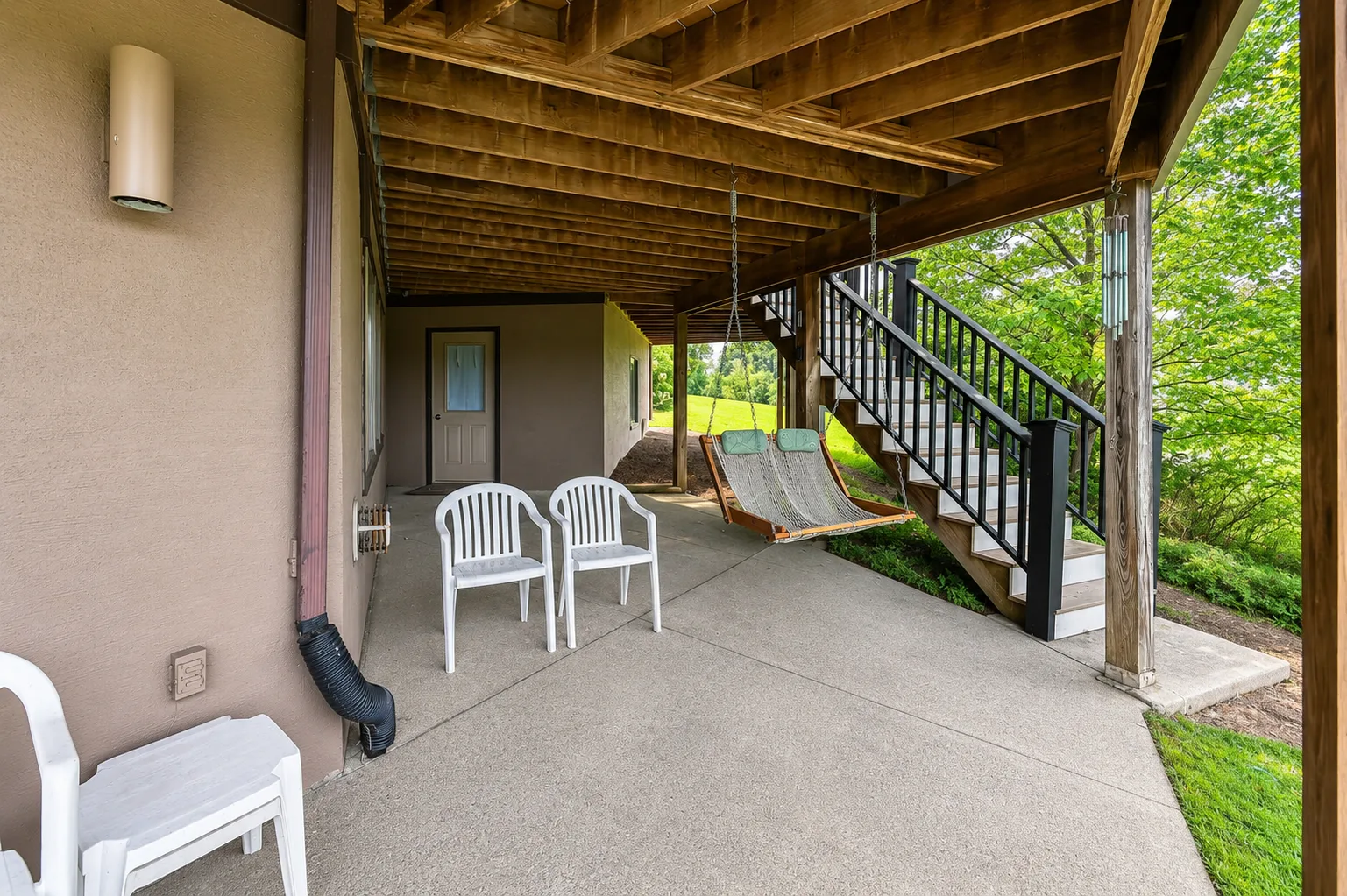 Un patio cubierto con asientos blancos y un columpio colgante junto a una escalera exterior.