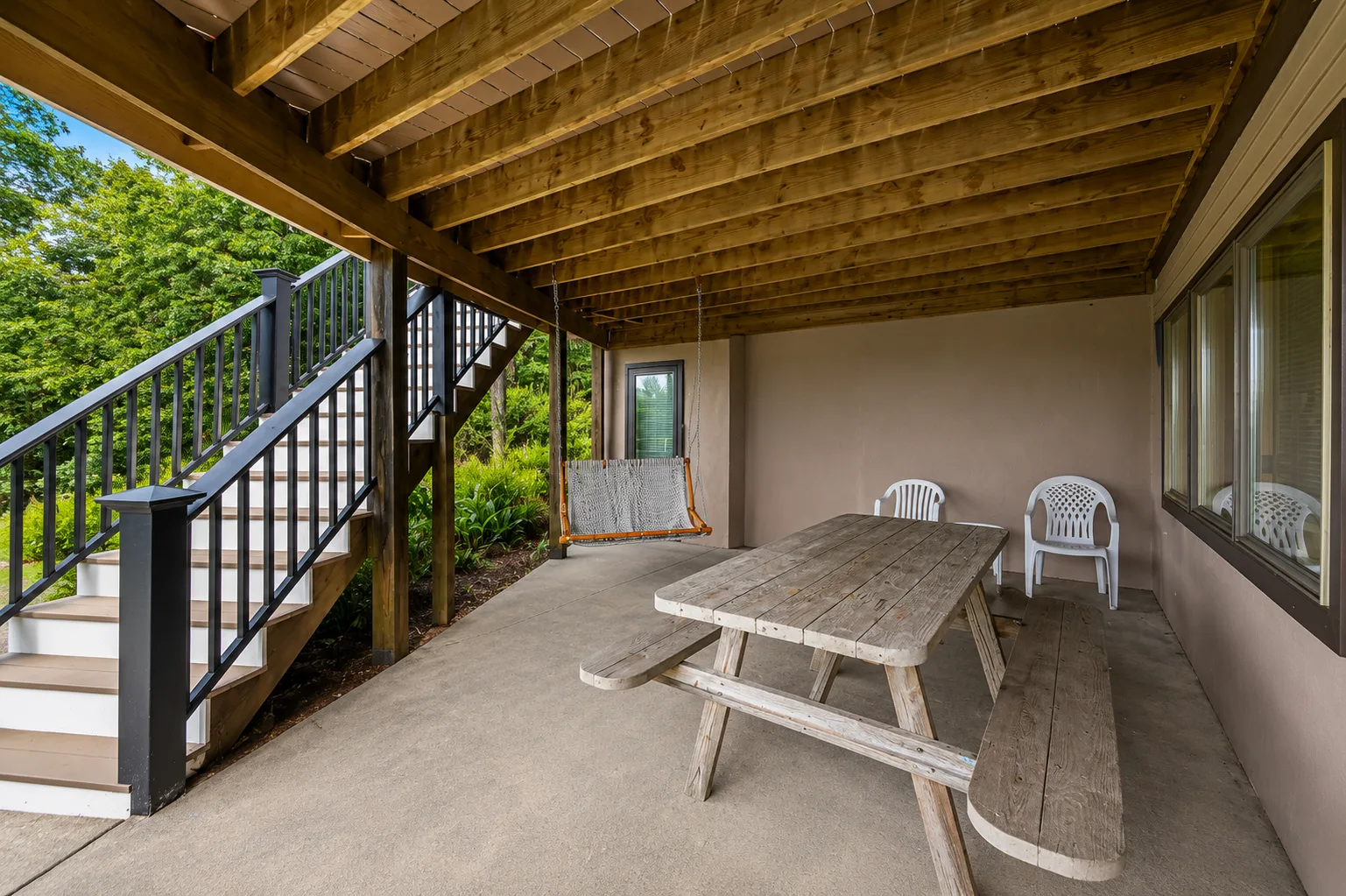 Un patio cubierto tiene una mesa de picnic, sillas y escaleras hacia un jardín.