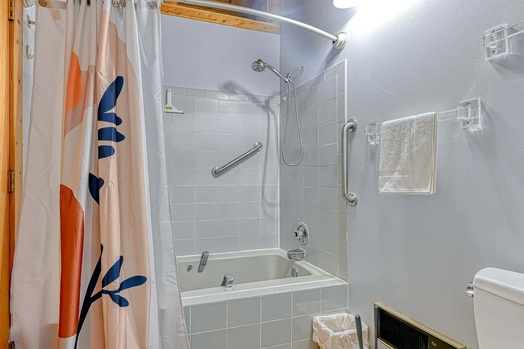 Un baño alicatado con bañera, accesorios de ducha y una cortina estampada.