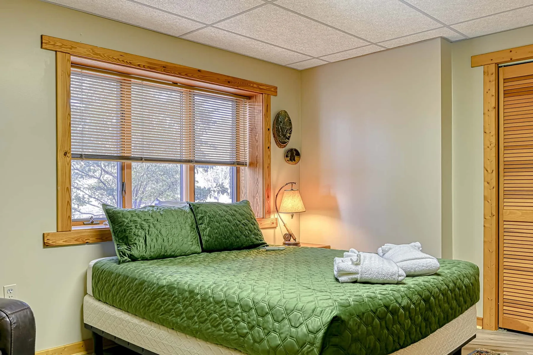 Un dormitorio con una colcha verde y una ventana con persianas.