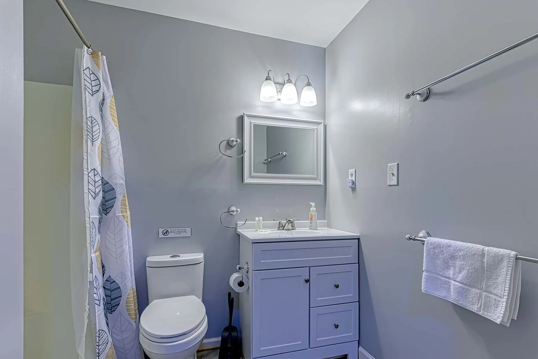 Un baño con lavabo, espejo, inodoro y cortina de ducha estampada.