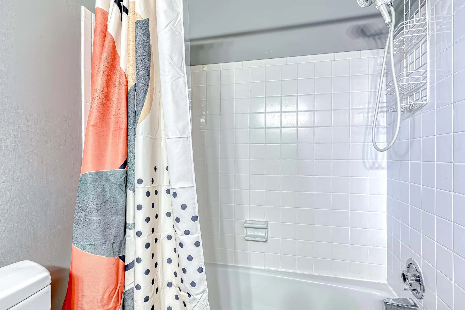 Una ducha de baño con azulejos, una cortina estampada y un cabezal montado en la pared.