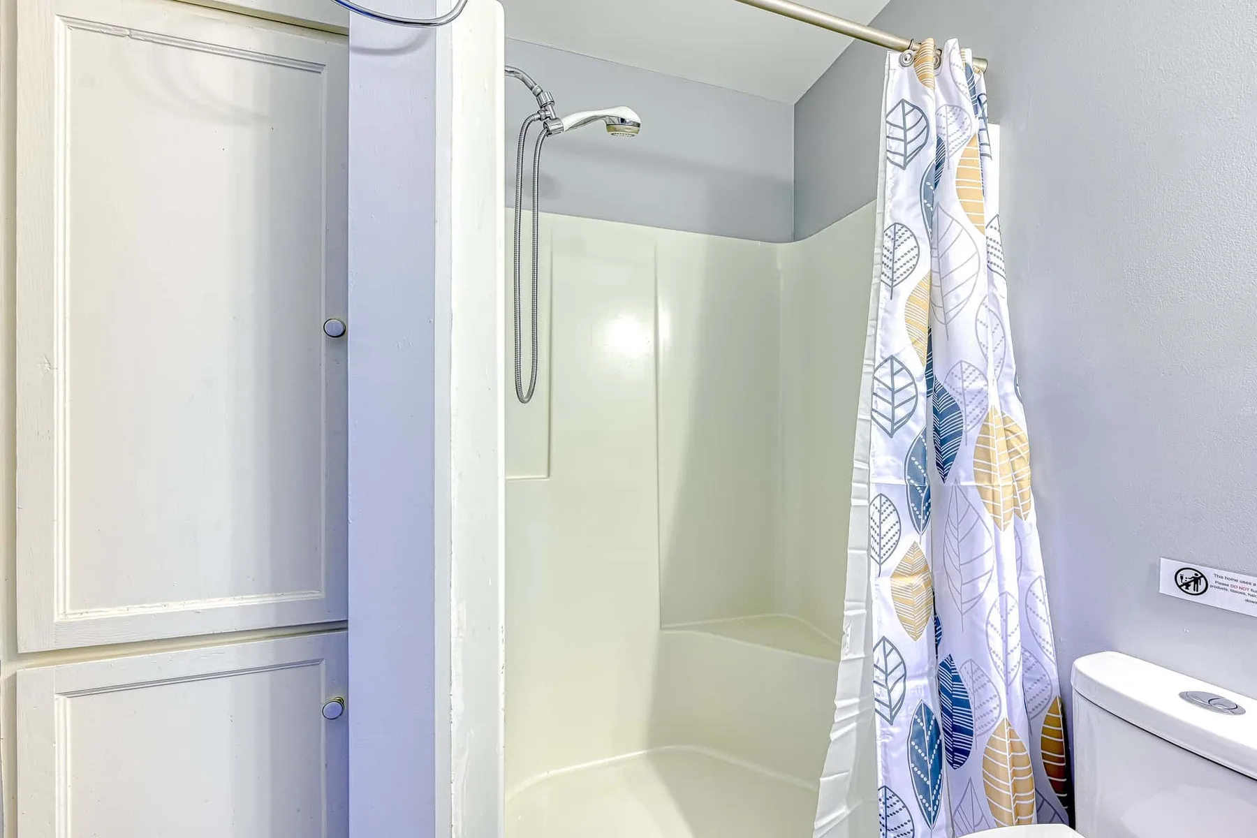 Un baño con bañera, cabezal de ducha y cortina estampada.