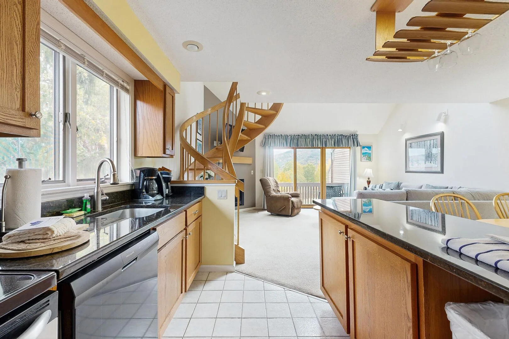 A bright open-plan kitchen and living area with a spiral staircase and large windows.