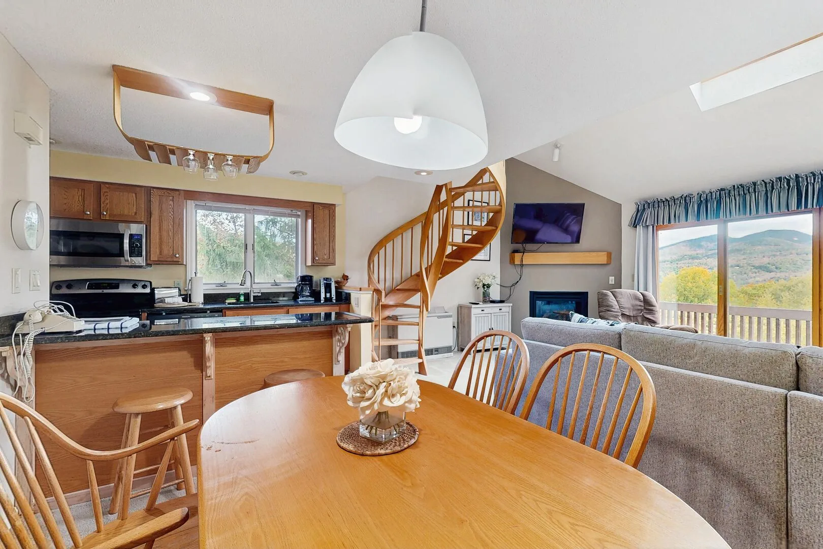 An open-plan living and dining area with a kitchen, staircase, and large windows.
