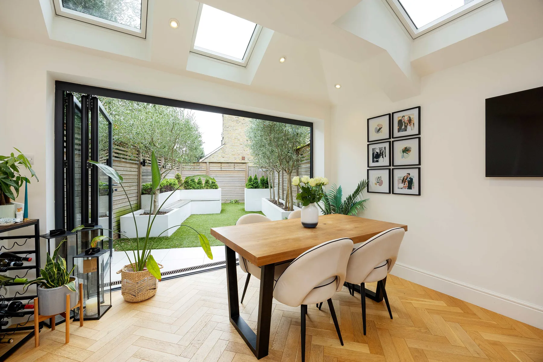 A bright dining area opens onto a garden through wide folding glass doors.