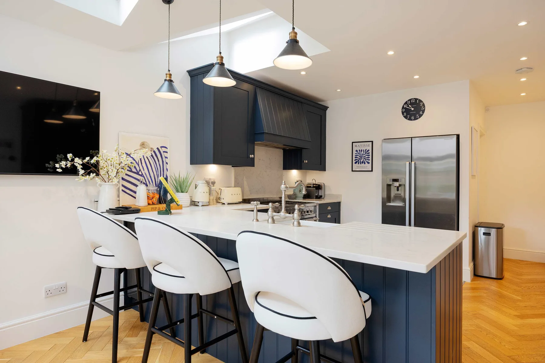 A modern kitchen features a long island with white seating and dark cabinetry.