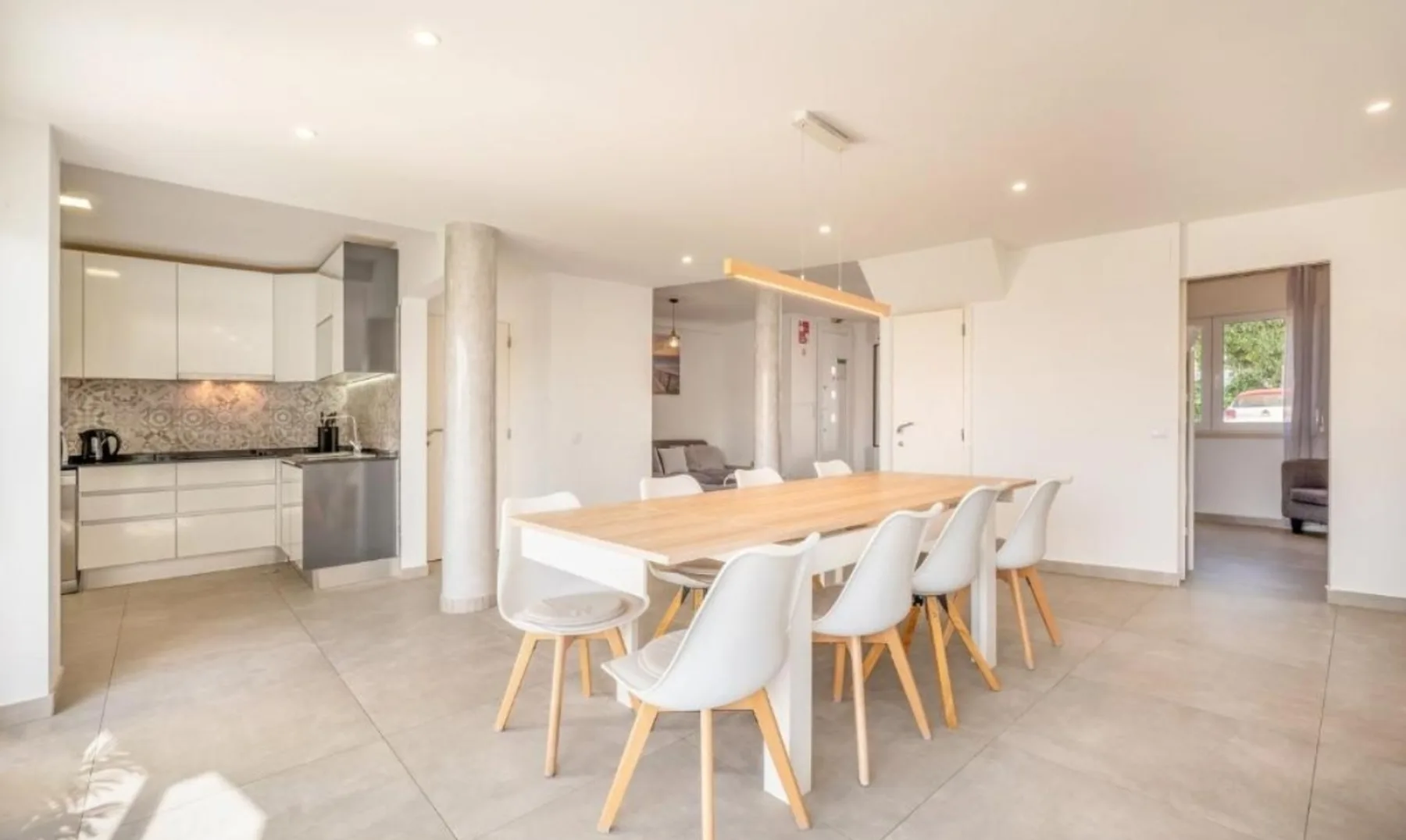 Un comedor diáfano y luminoso con una mesa larga y cocina contigua.