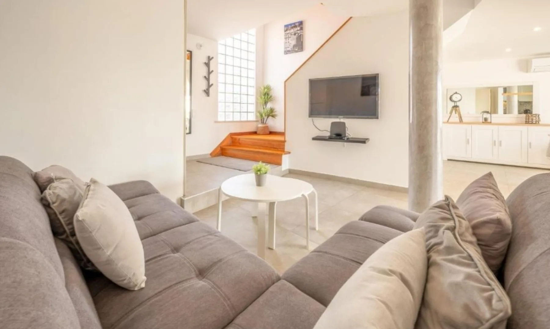A bright living room with seating, a coffee table, and a wall-mounted television.