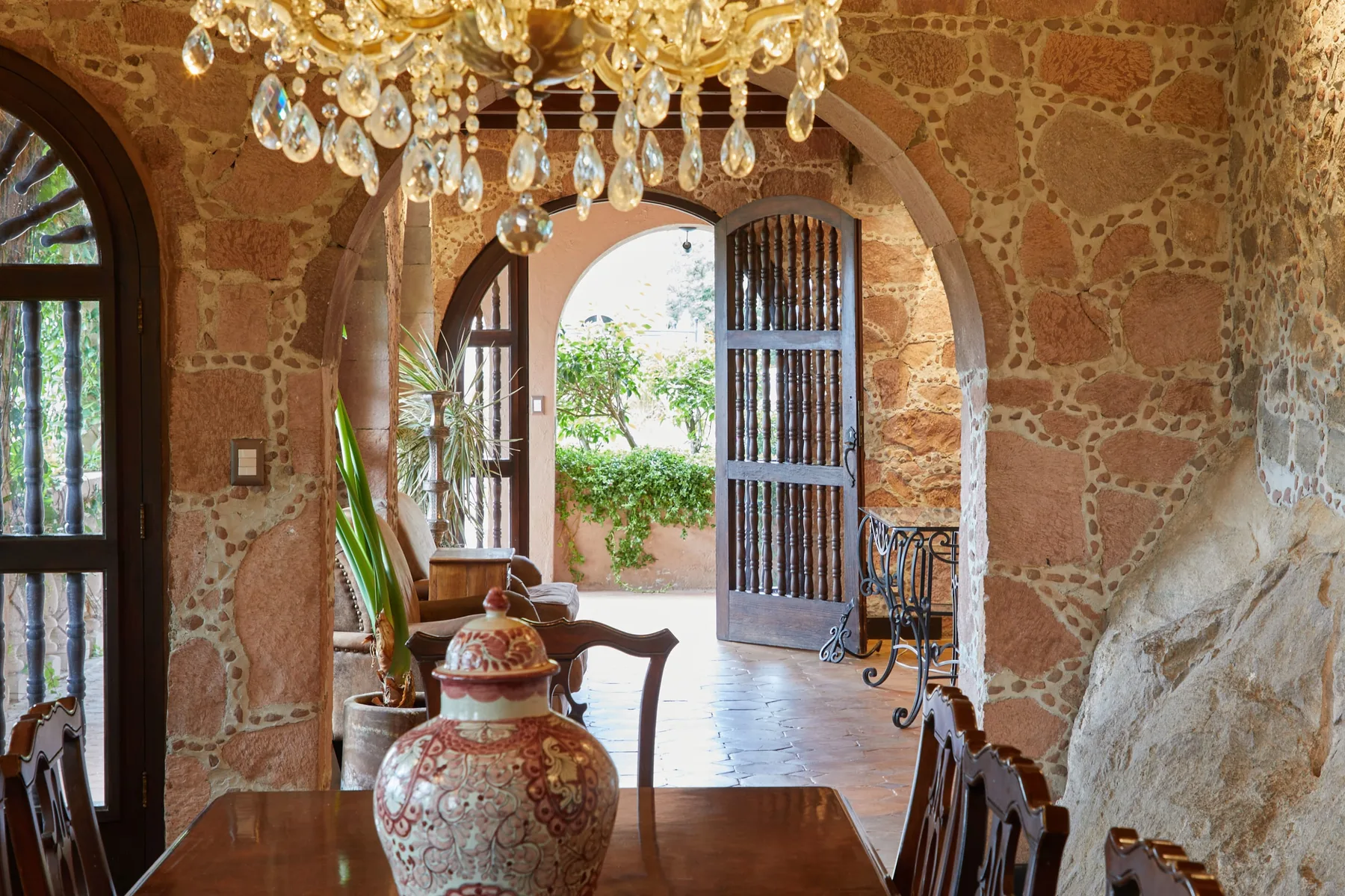 A stone dining room opens through an arched doorway to a leafy courtyard.