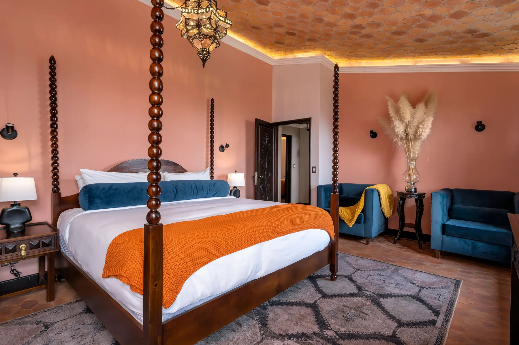 A bedroom with a wooden four-poster bed, blue seating, and patterned rugs.