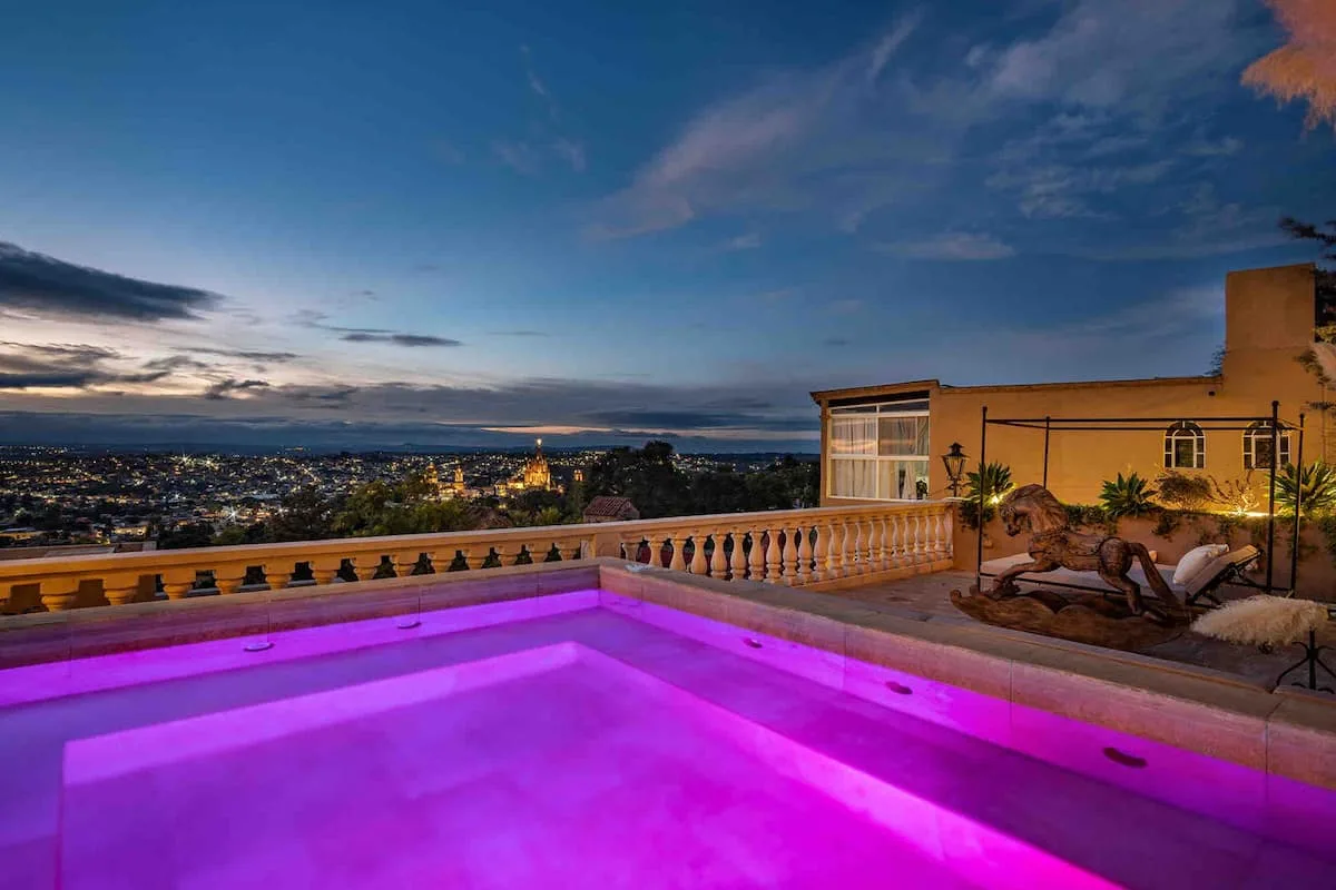 A glowing swimming pool overlooks a city at dusk.