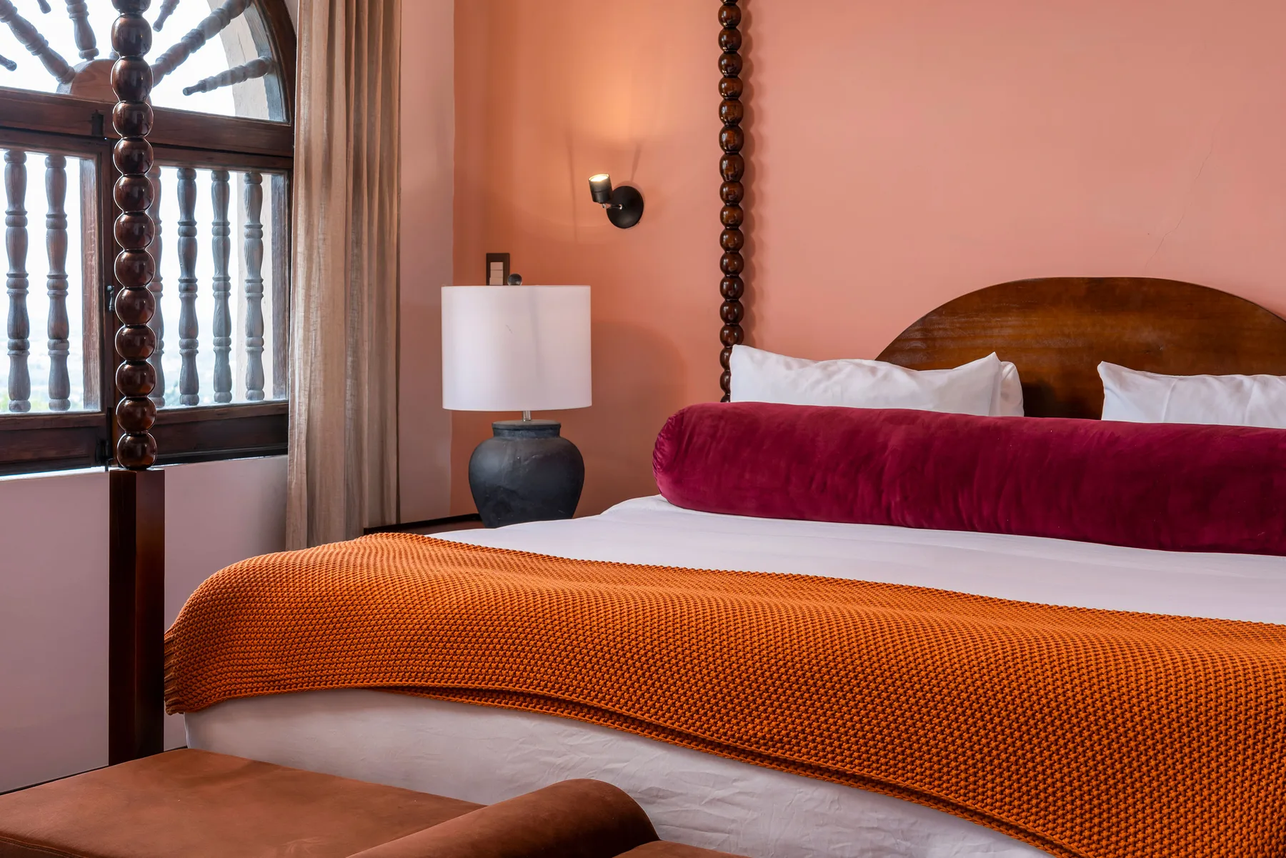 A bedroom with a bed dressed in white linens and an orange coverlet.
