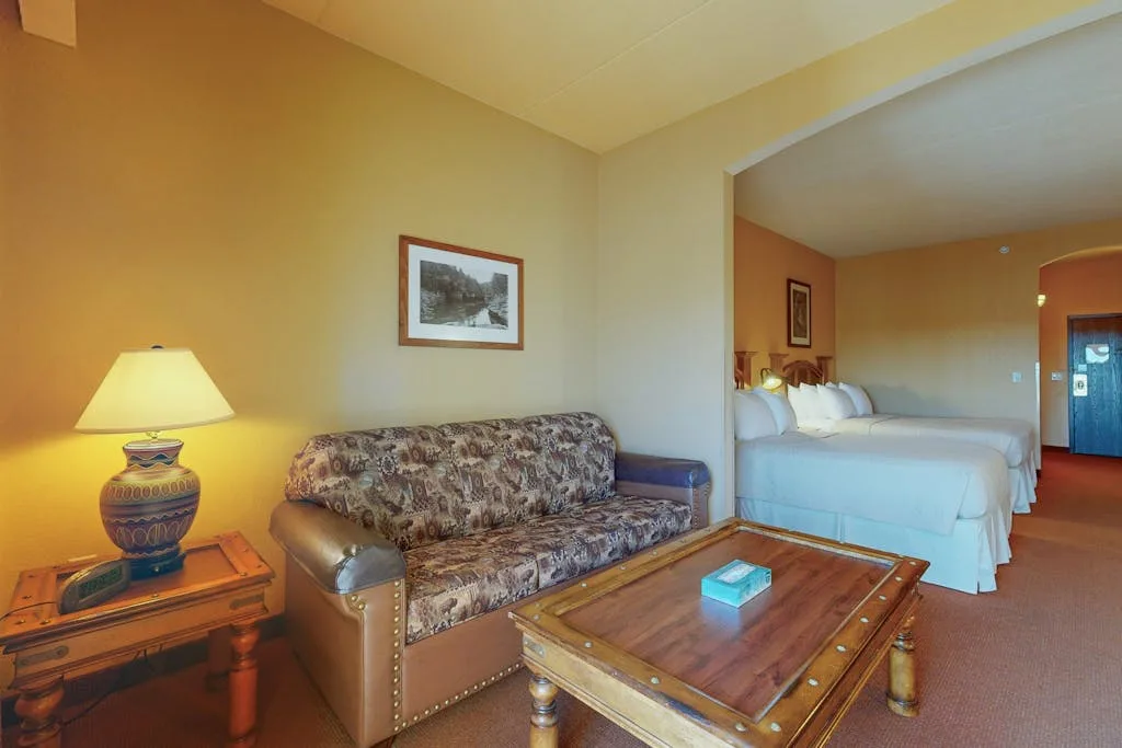 Una sala de estar con asientos estampados, una mesa de centro de madera y una cama al fondo.