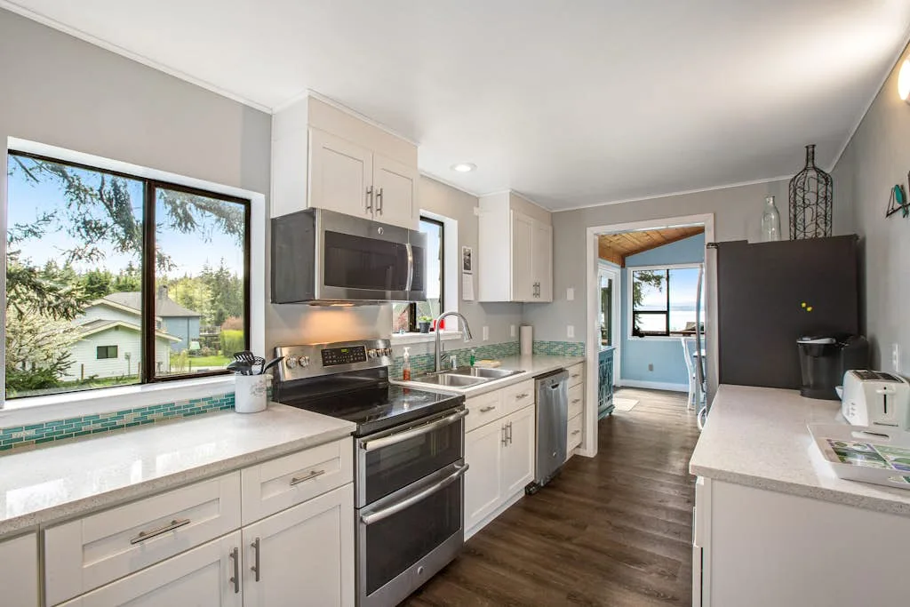 A bright kitchen with white cabinets, a stove, and a large window.