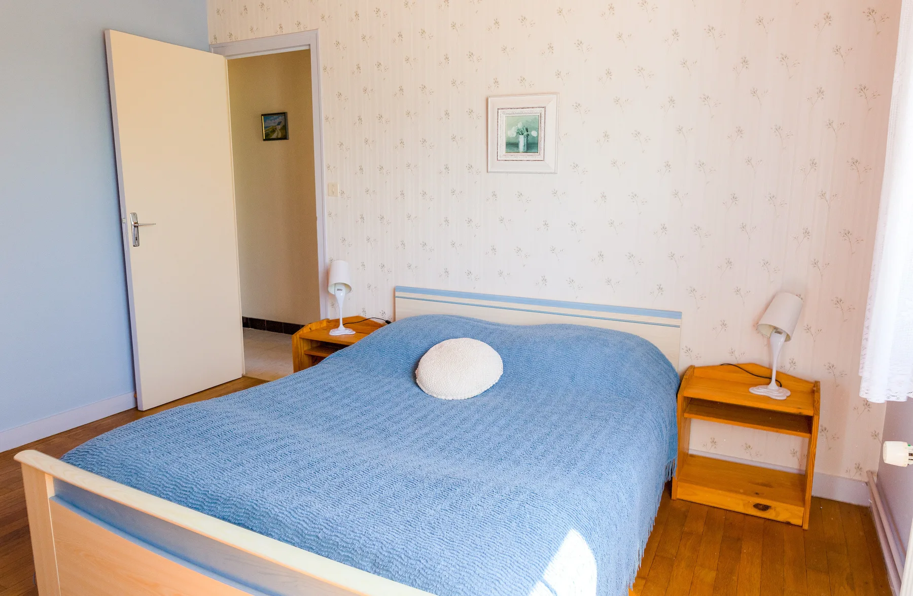A bedroom with a blue-covered bed and wooden bedside tables.