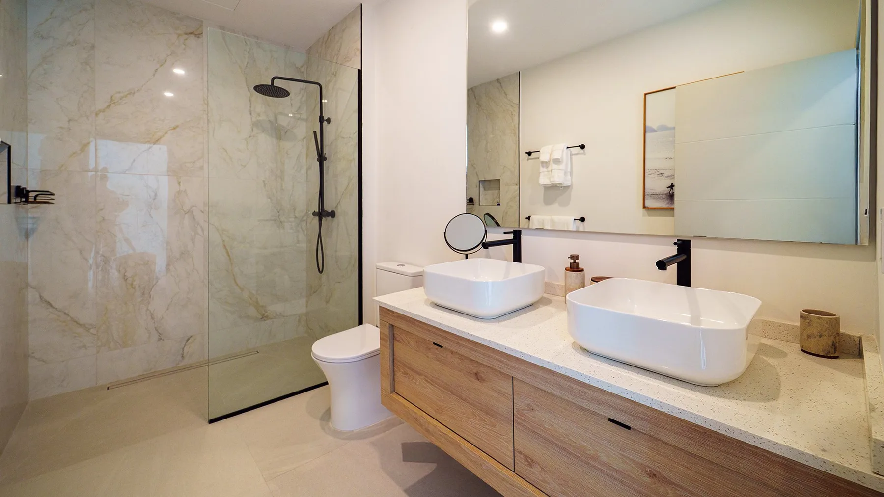 Un baño luminoso con ducha de vidrio, dos lavabos y un tocador largo.