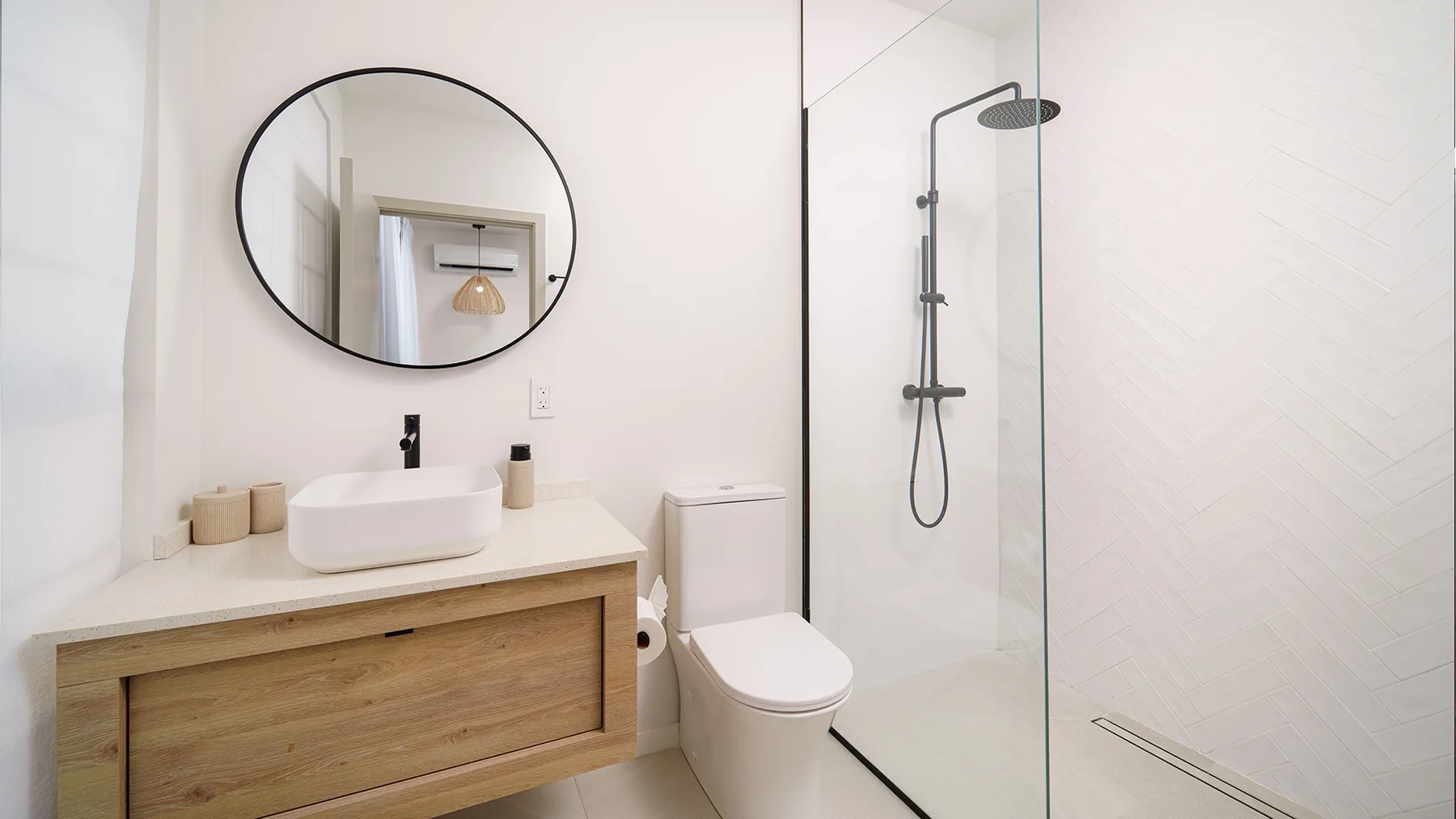 Un baño luminoso con un tocador en tono madera y una ducha de vidrio.