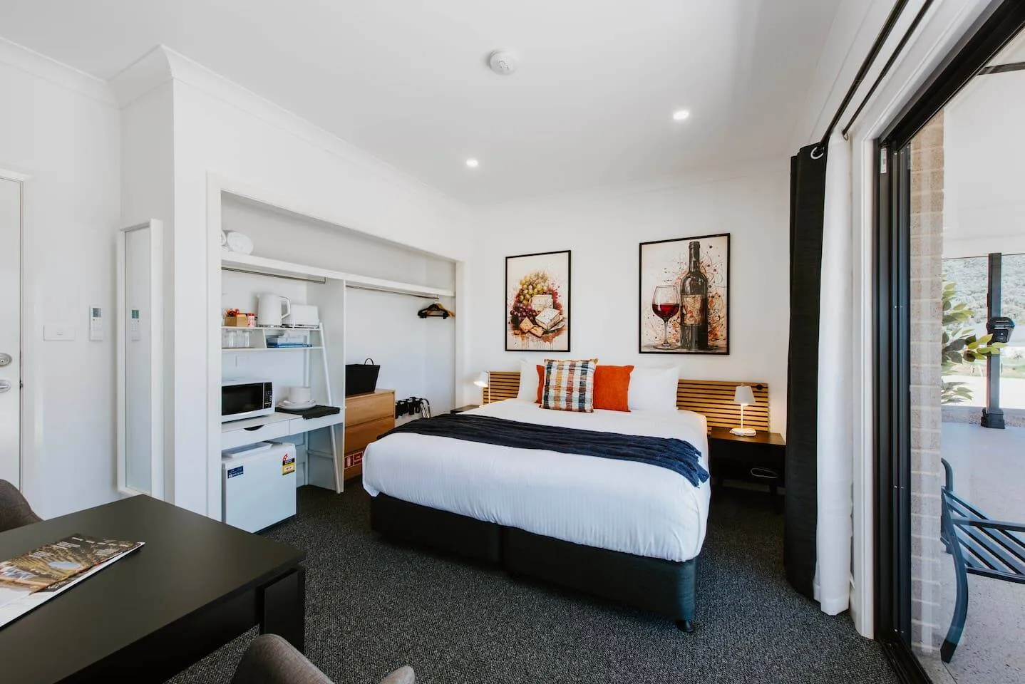 Un dormitorio con una cama, una cocina pequeña y puertas corredizas de vidrio hacia un patio.