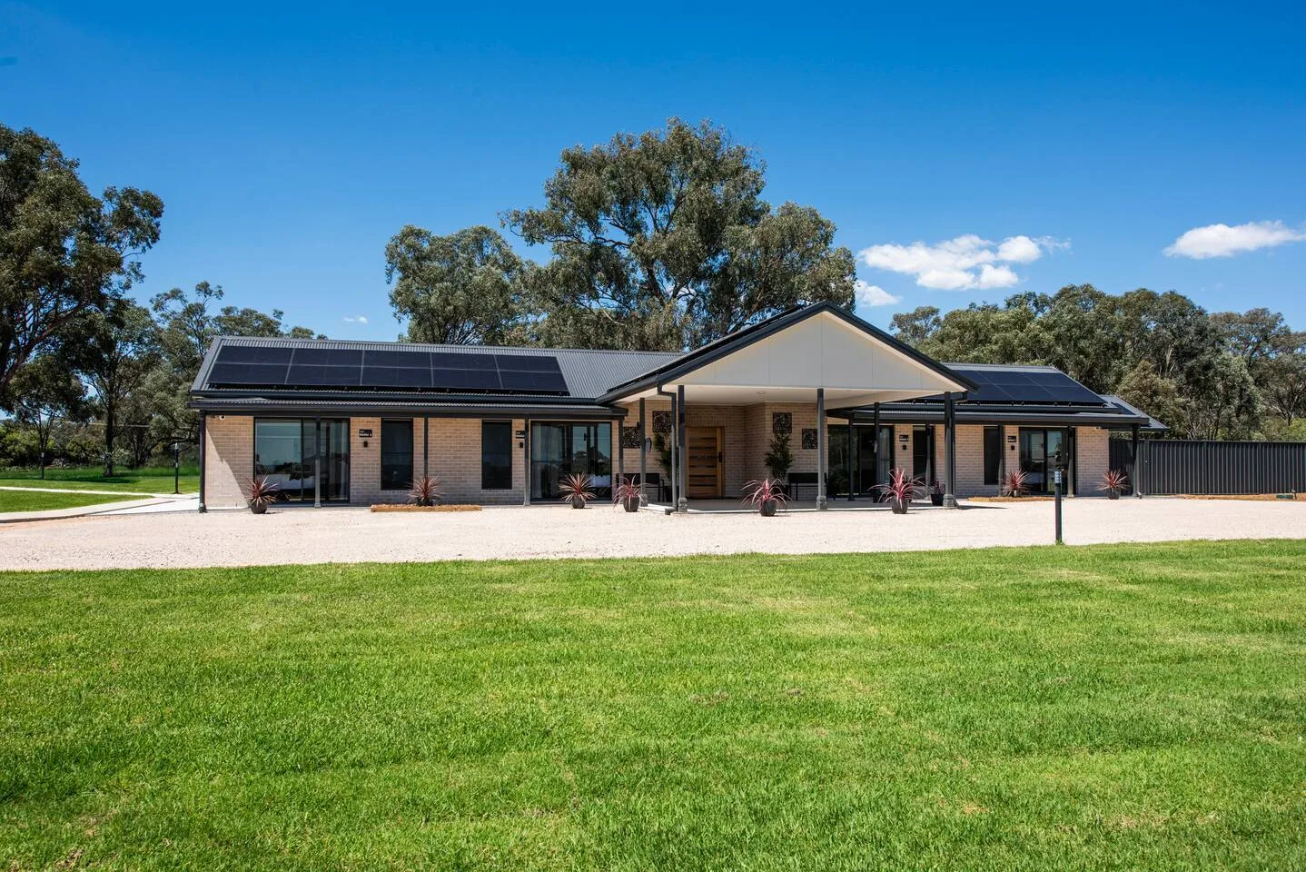 A modern single-story building stands beside a broad green lawn under a clear blue sky.