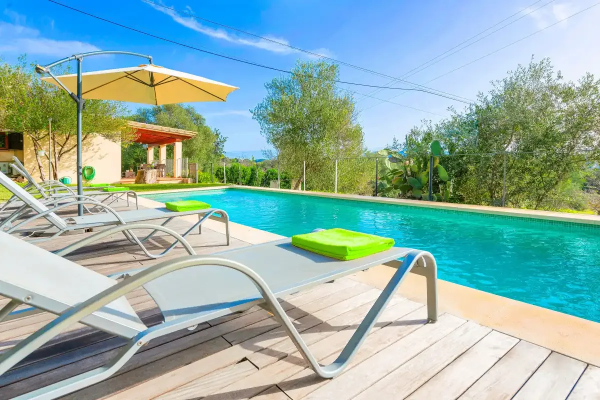 An outdoor swimming pool beside a wooden deck with lounge seating and a sun umbrella.