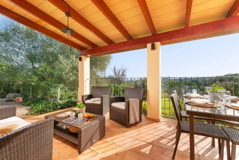 A covered patio has wicker seating and a dining table overlooking greenery.