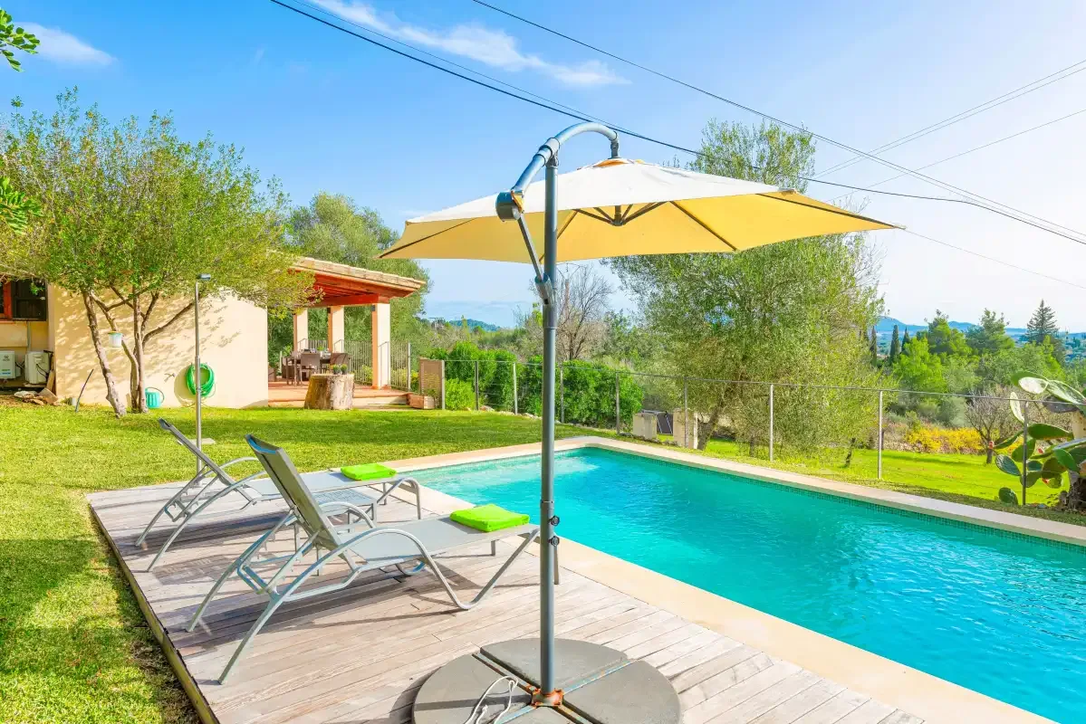 An outdoor swimming pool beside a wooden deck and a large sun umbrella.
