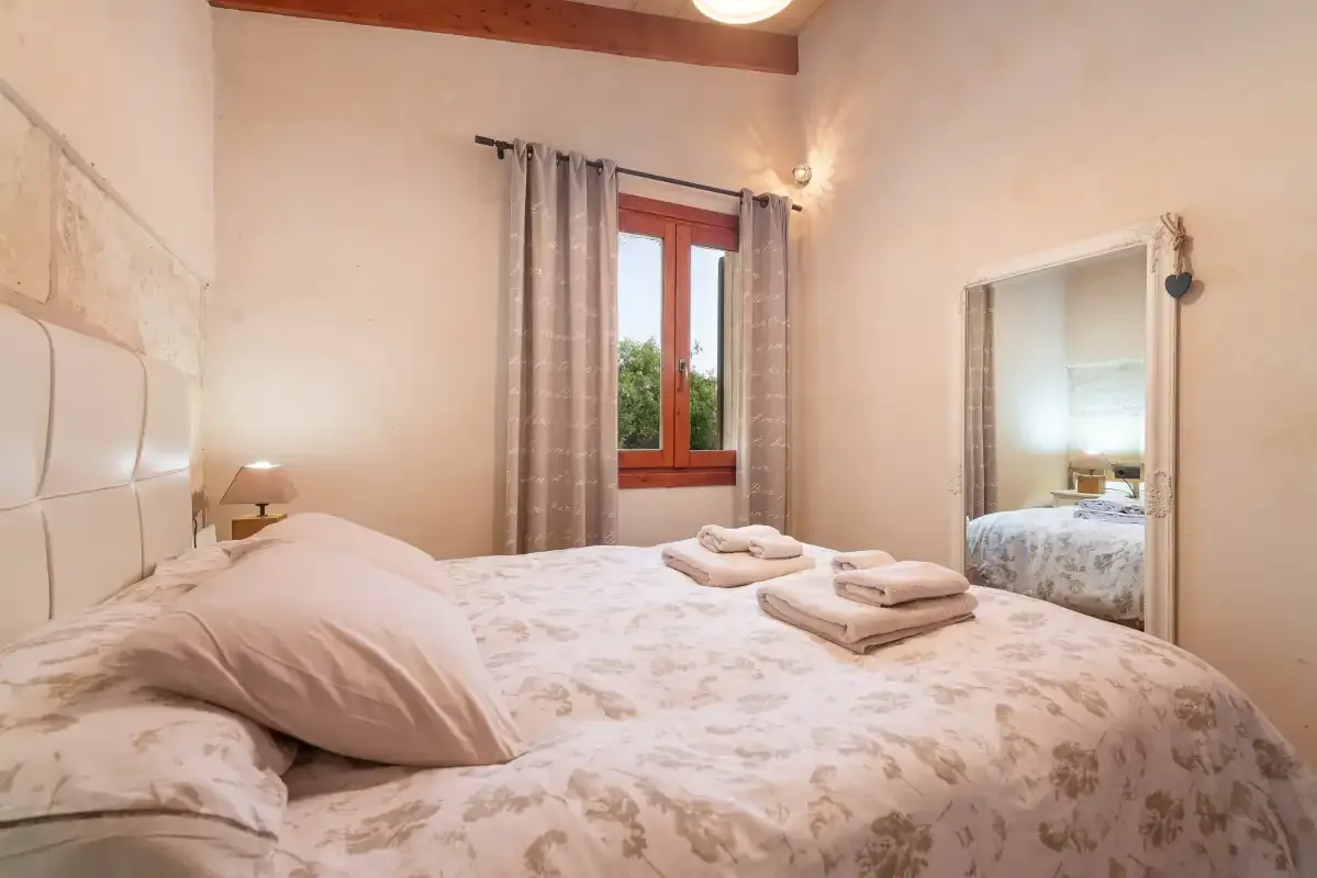 A bedroom with a bed, folded towels, and a window with curtains.