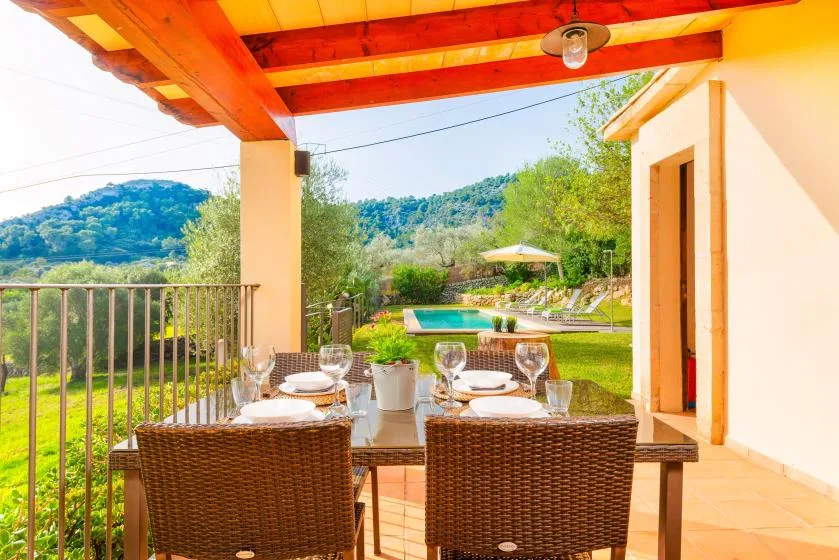 A covered outdoor dining area overlooks a garden and swimming pool.
