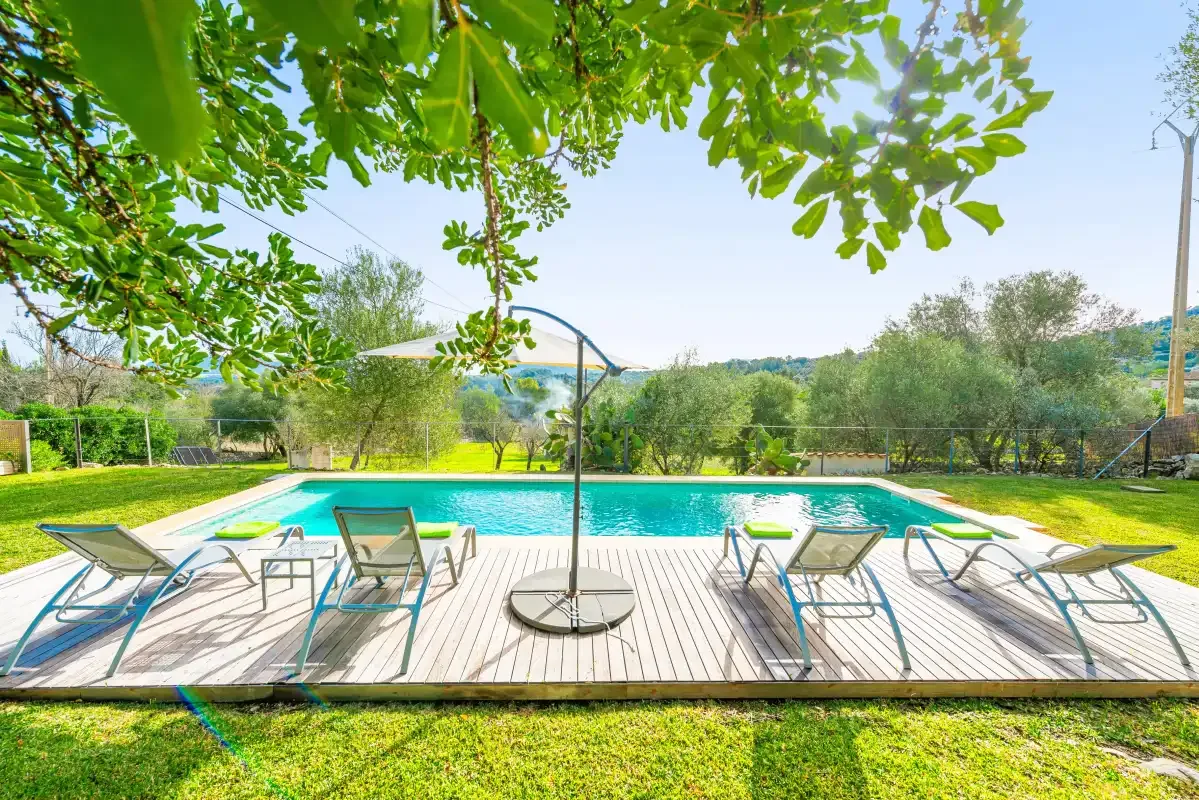A swimming pool with lounge seating sits beside a wooden deck and grassy lawn.