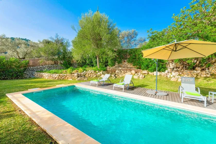 A swimming pool beside a wooden deck with loungers and a large umbrella.