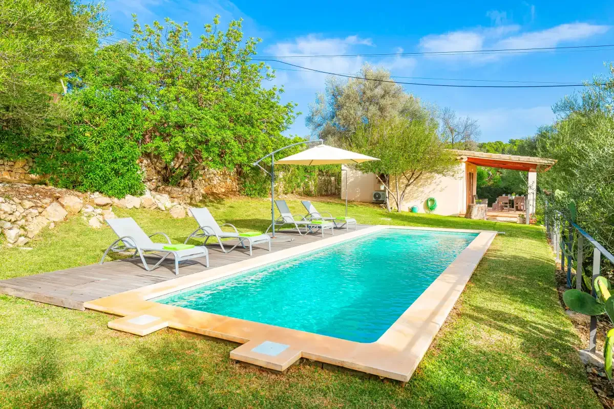 An outdoor swimming pool sits beside a grassy garden with lounge seating.