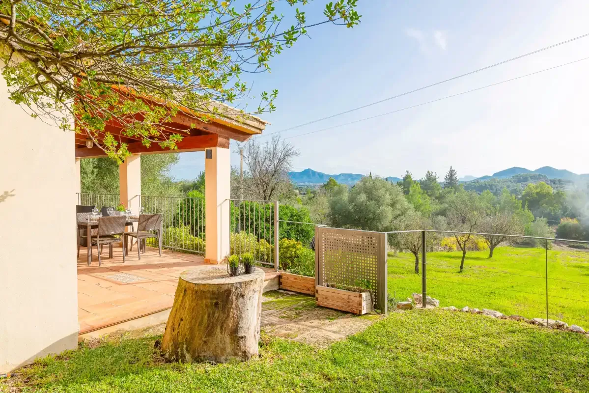 A covered patio with outdoor seating overlooks a green garden and distant hills.